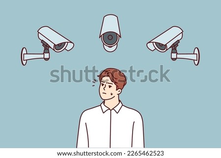 Embarrassed man stands among cameras recording every step of city dwellers to prevent commission of crimes. Dissatisfied man looking at CCTV cameras wondering if Big Brother is spying 