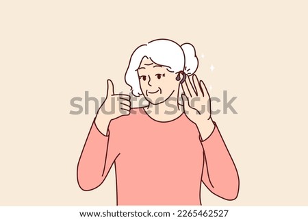 Elderly woman uses hearing aid and shows thumbs up confirming good sound volume thanks to new device. Gray-haired old lady with hearing aid enjoys opportunity to hear others and communicate freely 