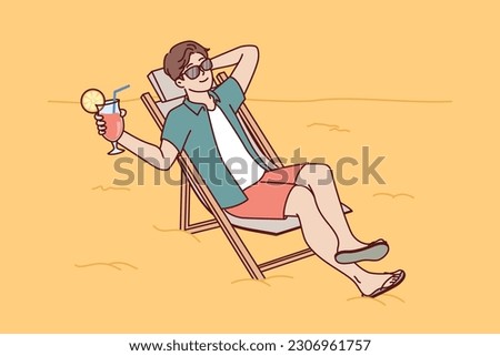 Man tourist is sunbathing on beach sitting in sun lounger and drinking fruity refreshing cocktail. Guy tourist and travel lover sunbathes spending vacation on beach of sunny ocean. 