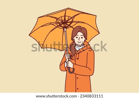 Woman with umbrella is dressed in oilcloth coat so as not to get wet from rain on autumn walk. Happy girl holding umbrella and looking at screen offering to take walk during rainy weather