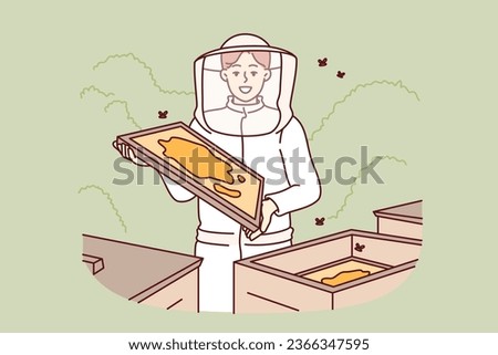 Woman beekeeper stands in apiary among hives and flying bees, takes out honeycombs with honey, dressed in white protective suit. Girl farmer works in apiary, producing ecological food