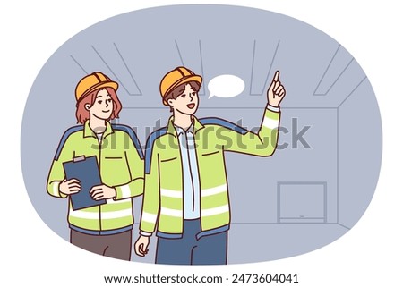 Two industrial room engineers discussing production process and how to repair equipment. Man and woman engineers in construction uniforms and safety helmets hold meetings in unfinished building