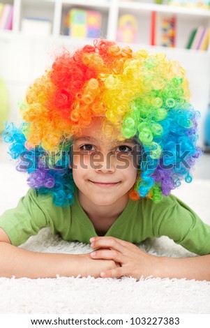 Young boy with clown wig laying on the floor smiling
