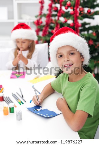 Kids making christmas and seasonal greeting cards in front of the decorated tree