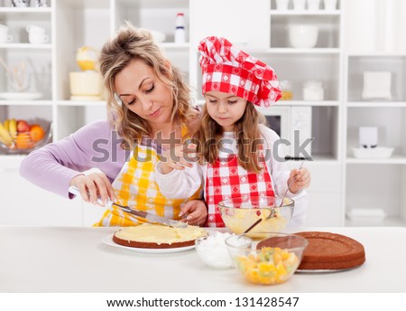 Mother and little girl making a cake together - spreading the filling