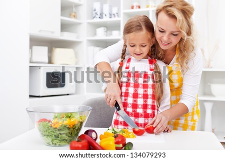Woman and little girl preparing a vegetables salad in the kitchen