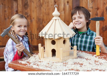Happy kids building a bird house - smiling and holding hammers