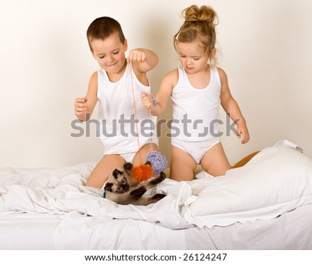 Kids playing on the bed with a kitten and yarn balls