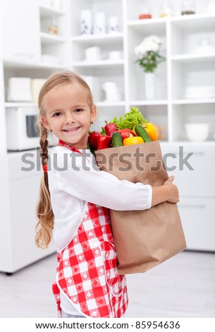 Happy healthy girl with apron in the kitchen holding groceries bag