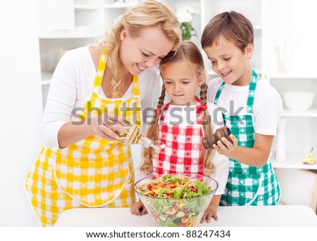 Family in the kitchen seasoning the fresh vegetables salad