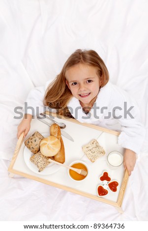 Happy little girl having a light breakfast in bed - top view
