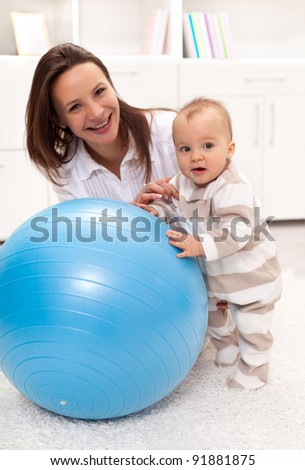 Baby girl stands by a large ball with a little help from her mother