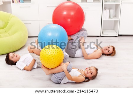 Kids and their mother exercising at home using large gymnastic balls