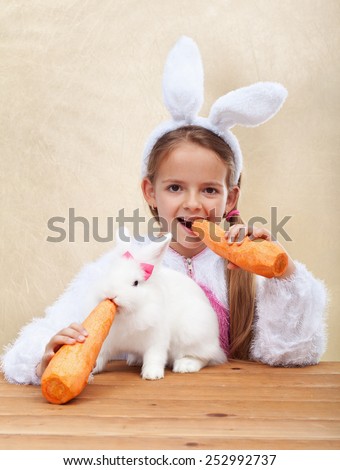 Bunnies eating large carrots - little girl with bunny ears feeding her white rabbit - shallow depth of field