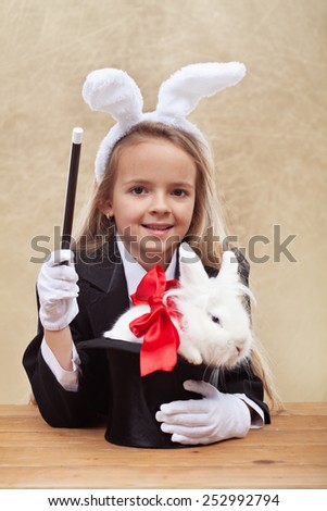 Happy magician girl wearing bunny ears holding white rabbit in a hat- shallow depth of field
