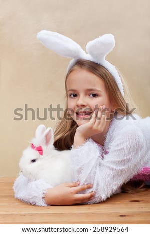 Happy girl in bunny costume holding her white rabbit - laying on wooden floor