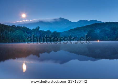 Landscape of lake just off the Blue Ridge Parkway in North Carolina in the early morning blue hour with moonlight and trees reflecting in the calm and serene water.