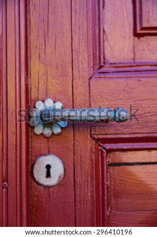 Image of a red door with ornate bronze handle. Shallow depth of field.