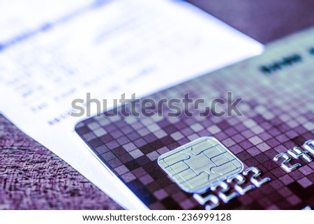 Credit card and check from shopping on the table, focus on the microchip of the card. In blue tone