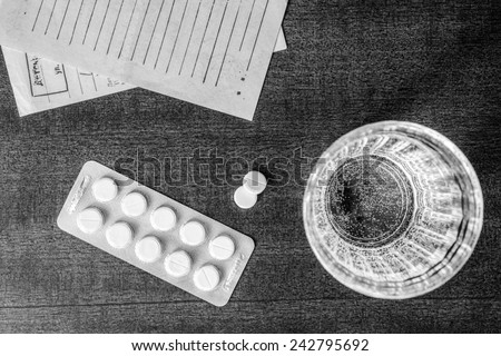 Cure the disease, tablets with a glass of water and prescriptions from the doctor on the table. Top view, in the black and white colors