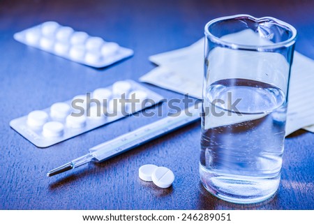 Cure the disease, a tablets  with a glass of water and prescriptions from the doctor on the table. Angle view, focus on the tablets, in blue tones