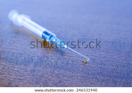 Medicine flows from the syringe and spread out on the table. Angle view, in blue tones