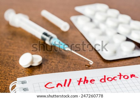 Call the doctor, medicine flows from the syringe and spread out on the table, lies next to the pills. Angle view, focus on the sign