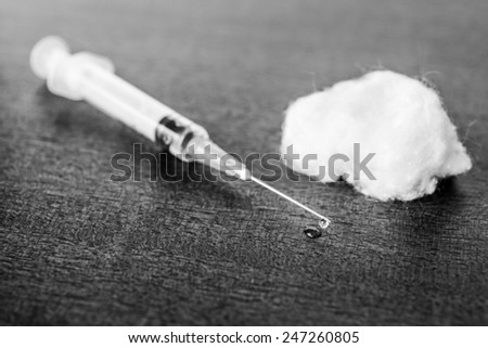 Medicine flows from the syringe and spread out on the table, lies next to a cotton swab. Angle view, in black and white tones