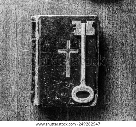 Key and Bible on the wooden desk with a candle. In black and white tones