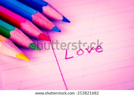 Word love written in a notebook with colored pencils. Image in red toning