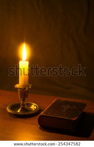 Old bible and candle on a wooden table. In warm toning