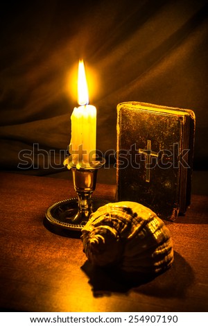Old bible and candle with sea shell on a wooden table. Focus on the bible, image vignetting and in yellow toning