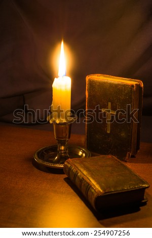 Bible and old book and candle on a wooden table. Focus on the bible