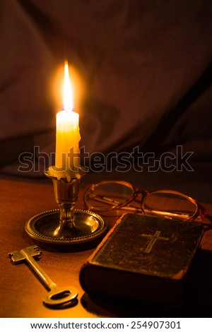 Old bible and candle with glasses on a wooden table. Focus on the candle