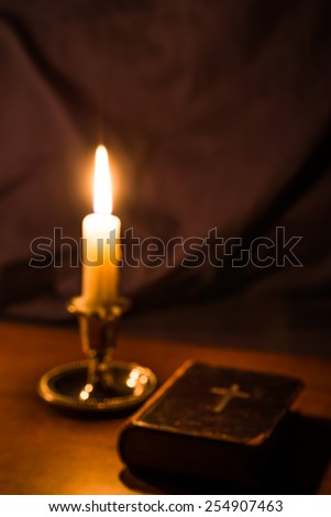 Old bible and candle on a wooden table. Image is out of focus