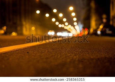 Nights lights of the big city, the night avenue with road markings and headlights of the approaching cars, close up view from asphalt level