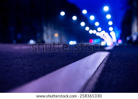 Nights lights of the big city, the night avenue with road markings, close up view from asphalt level. In blue tones