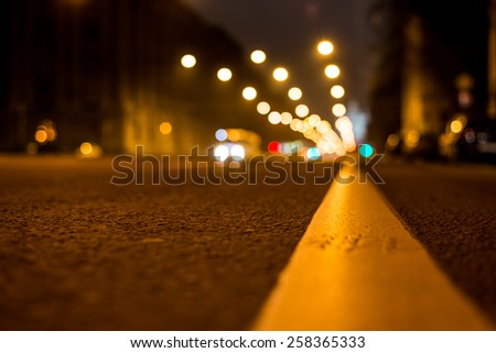 Nights lights of the big city, the night avenue with road markings and headlights of the approaching car, close up view from asphalt level