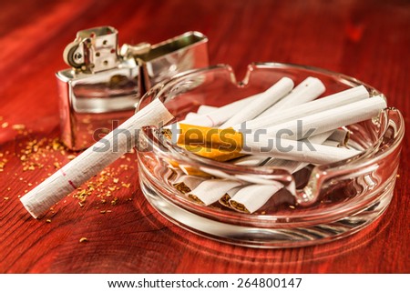 Cigarettes in the ashtray, lighter stands next, on the table broken up tobacco. Focus on the cigarette