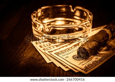 Cuban cigar with glass ashtray on a several dollar bills on the table. Image vignetting and the yellow-orange toning