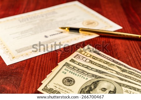 Several dollar bills and golden pen with bank check on the table. Focus on the dollars