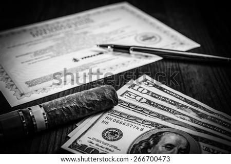 Cuban cigar on a several dollar bills and golden pen with bank check on the table. Focus on the cuban cigar, image vignetting and black and white tones