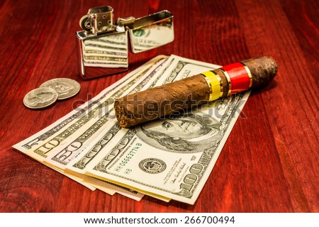 Cuban cigar on a several dollar bills and also coins and lighter on the table. Focus on the cuban cigar