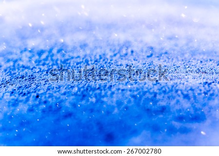 Shiny snowflakes on the surface close up under sunlight in the perspective. Image in the blue toning