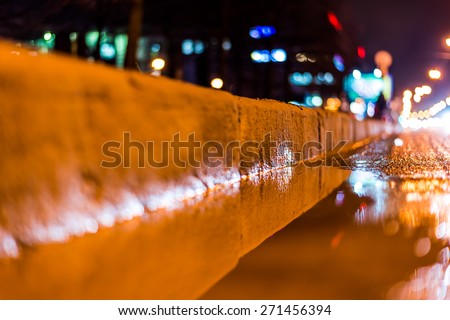 Night city after rain, a reflection of the city at night in the water. View of the stream of cars from the roadside at the asphalt level