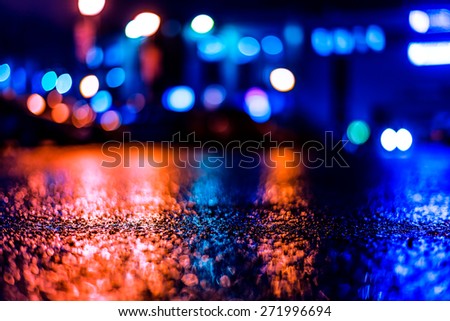 Shop windows are reflected on the wet asphalt after rain. View from the level of asphalt, image in the blue-purple toning