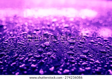Raindrops on the metal surface in the light colored lights. Image in the purple-blue toning