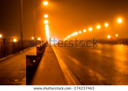 The bright lights of the city at night, the headlights of the approaching cars on the road bridge. View of the highway with a dividing border