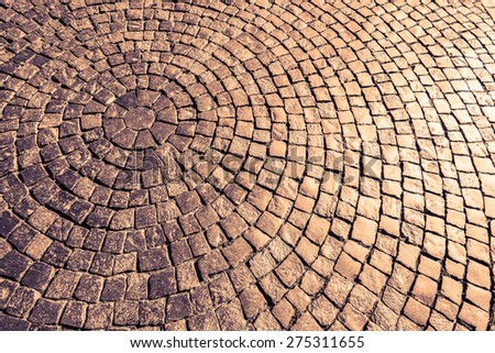 Ancient cobblestone paved circle on the pavement under the sunlight. Image in the orange-purple toning