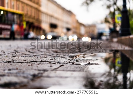 City central square paved with stone after a rain on which riding car. View from the pavement level next to the roadside puddle